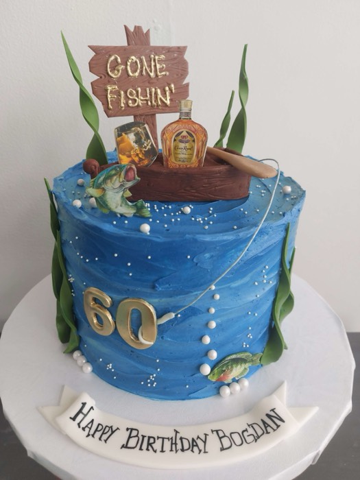 Blue textured buttercream 60th birthday fishing cake with Gone Fishin wooden sign, fishing rod, Crown Royal bottle, green seaweed, fish, and gold 60
