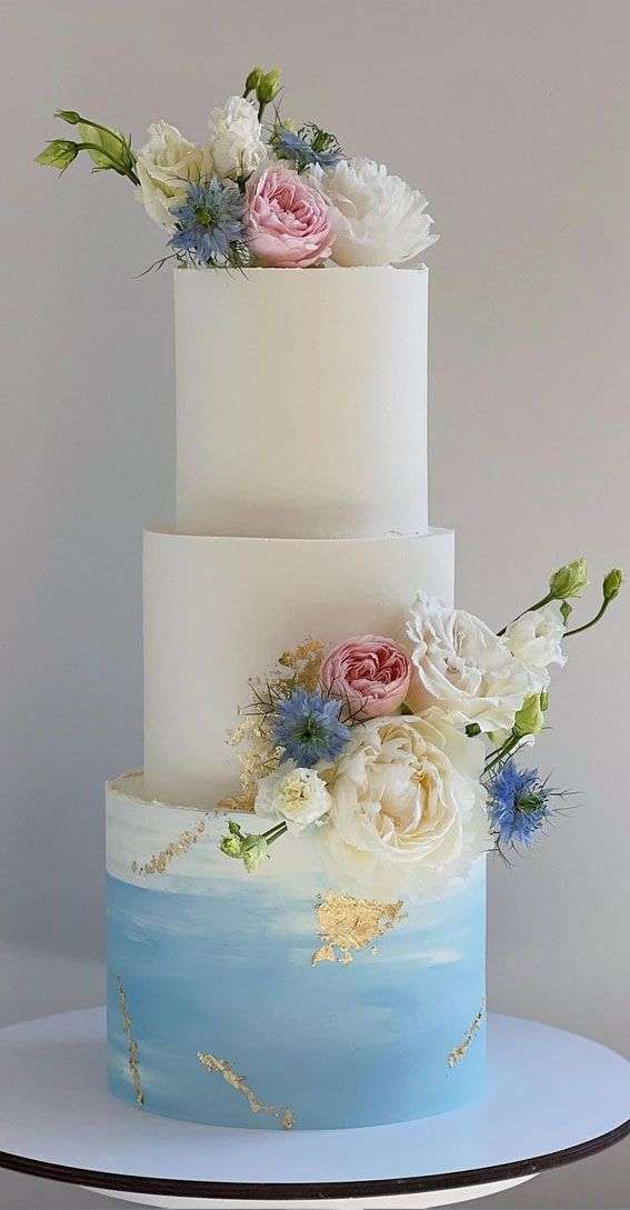 Three-tier white and blue ombre cake with fresh pink peonies, white garden roses, blue nigella flowers, and gold leaf accents